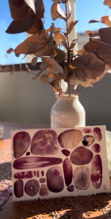 Un vase blanc contenant des branches sèches, avec des pierres colorées en arrière-plan.