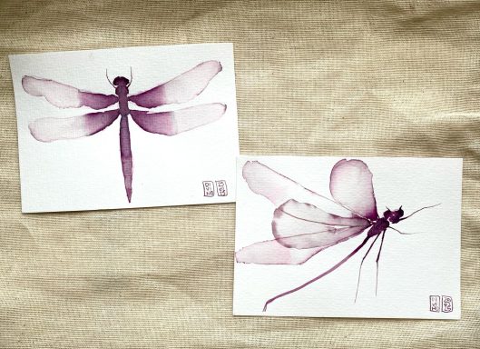 Deux aquarelles au vin de libellules avec des teintes violet pâle sur un fond blanc.