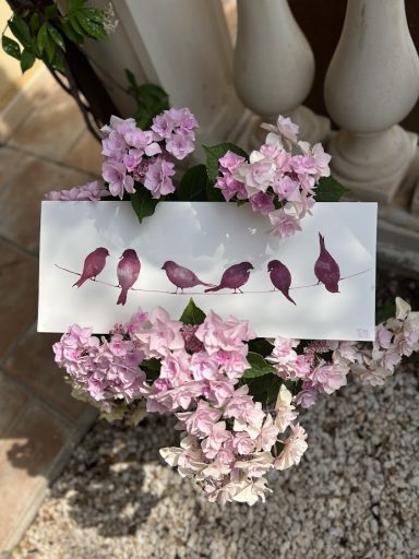 Trois oiseaux violets stylisés posés sur une carte blanche, entourés de fleurs roses.